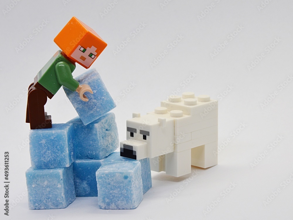 Fototapeta premium LEGO Minecraft Alex is building igloo from ice looking light blue scented stearine wax cubes, Minecraft polar bear is sniffing one of the cubes.