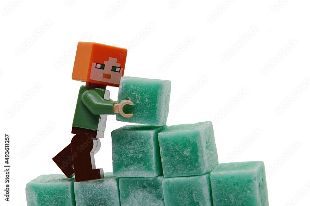 Naklejka premium LEGO Minecraft figure of Alex is building a wall from green coloured scented stearine wax cubes, white background