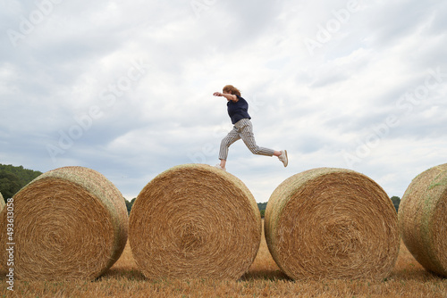 Photographie Adult woman jumping on some haystack of hay after harvesting in the field