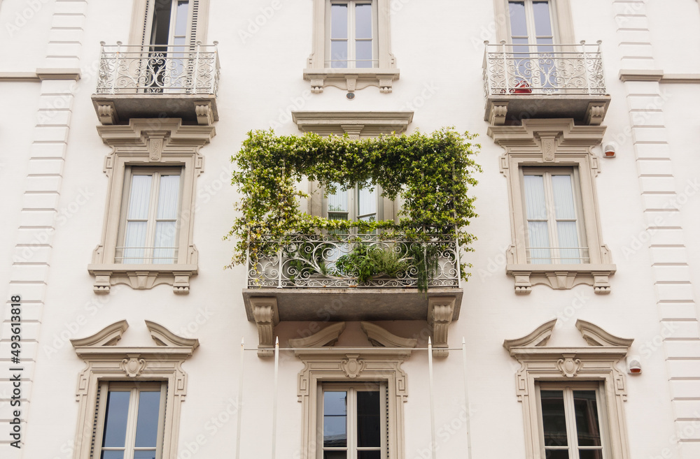 Balcony with weaving plants on a white facade in Milan, Italy