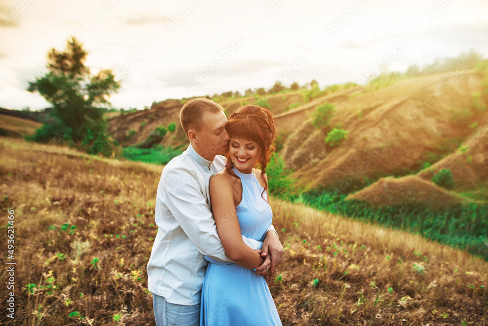 Young beautiful woman and man hug and kiss in nature at sunset.