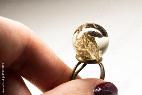 Hand holding an epoxy resin ring. Natural dried moss and small piece of lava preserved inside transparent ball. Selective focus on the details, blurred background.