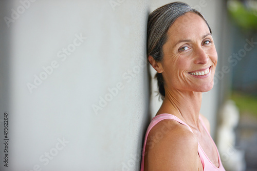 Happiness is an inside job. Portrait of an attractive mature woman in gymwear leaning against a gray wall. photo