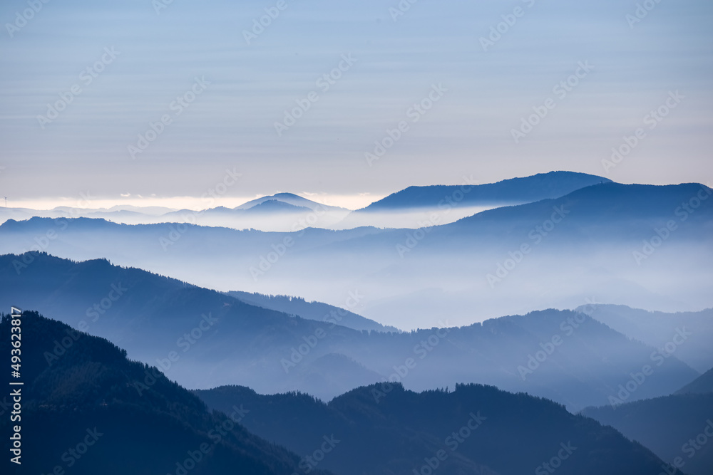 A panoramic view on the mountain peaks of the Hochschwab Region in Upper Styria, Austria. Cloudless weather on a sunny summer day in the Alps. Blue misty valley and soft hills. Concept freedom