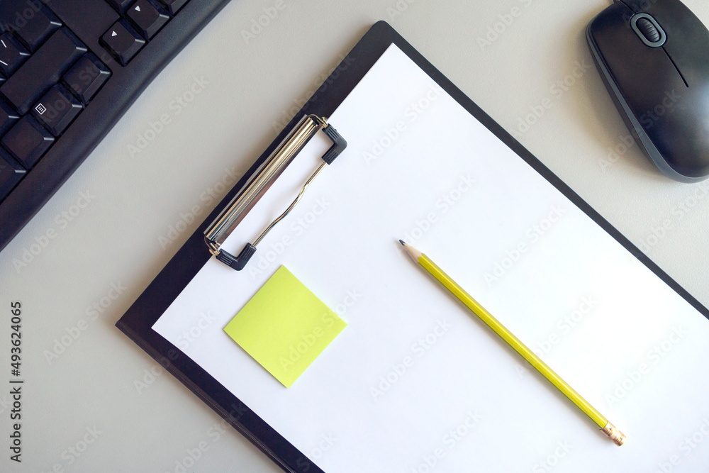 A folder for papers with a white sheet, a green sticker and a yellow pencil on a gray background with a black computer mouse and keyboard A folder for papers with a white sheet, a green sticker and a yellow pencil on a gray background with a black computer mouse and keyboard