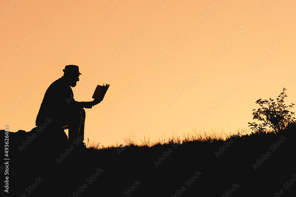 silhouette of man sitting on rock and reading book. reading books in nature