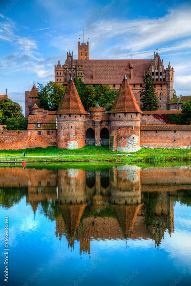 Obraz premium Malbork Castle Reflecting in the River Nogat, Poland, on a Calm Day