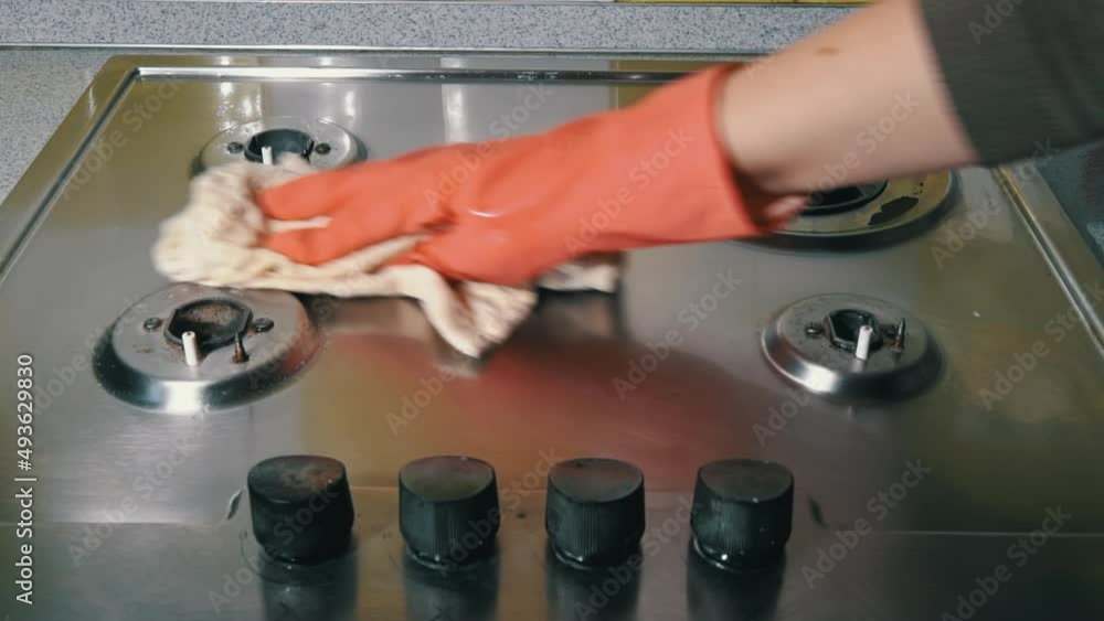 Woman in gloves washes and rubs a gas stove with detergent until it