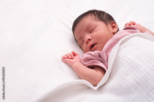 Close up portrait of cute adorable baby girl on white bed in bedroom. Newborn child relaxing and smiling in the bed in children nursery. Family morning at home.