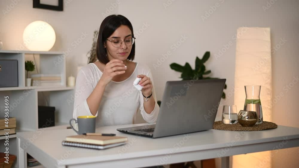 Woman putting airpods in her ears and using a laptop while having an online meeting Woman putting airpods in her ears and using a laptop while having an online meeting