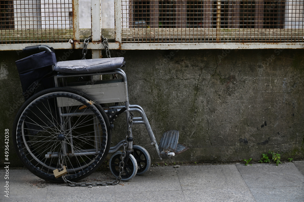 Old wheelchair parked on street with chain and lock Old wheelchair parked on street with chain and lock