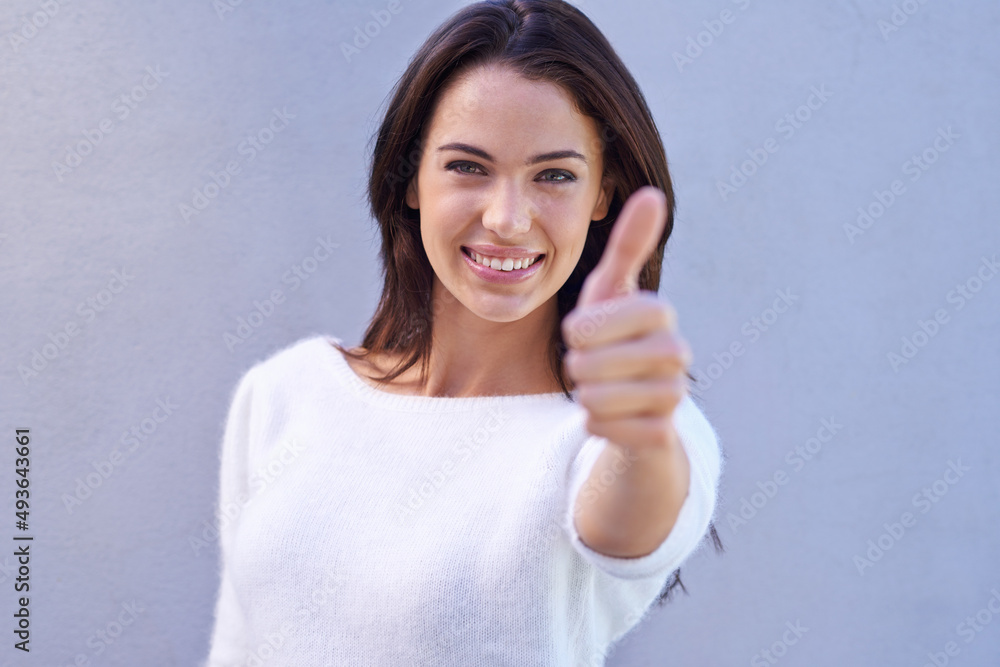 Youre good to go. Portrait of a happy young woman standing against a gray background and giving thumbs up. Youre good to go. Portrait of a happy young woman standing against a gray background and giving thumbs up.