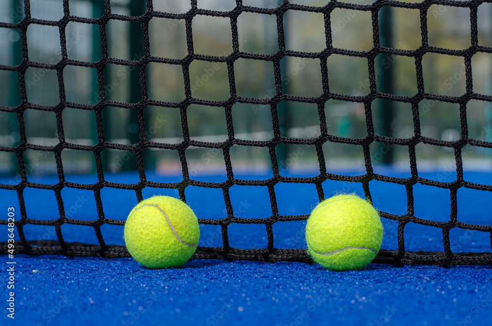 two paddle tennis balls over the service line and near the net of a blue paddle tennis court