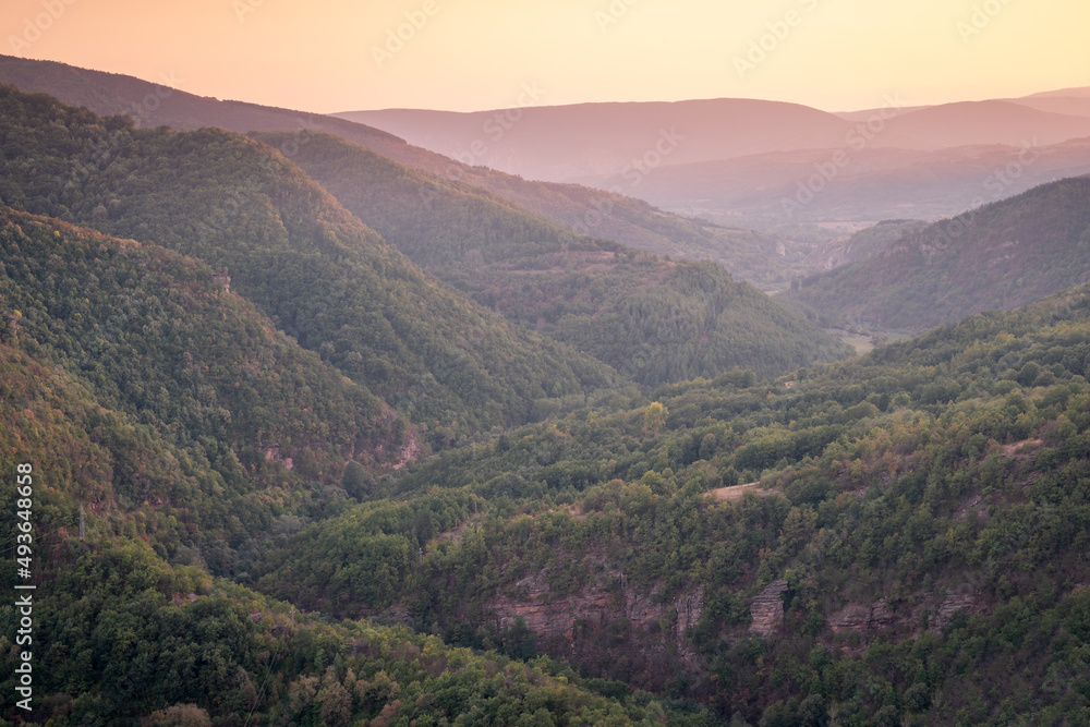 Golden hour view of a river canyon with hills covered by forests lighten by golden light on autumn