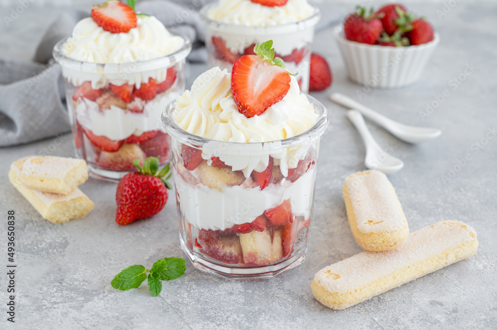 Strawberry tiramisu or trifle, dessert in a glass jar with fresh strawberry and mint leaves on a gray background Strawberry tiramisu or trifle, dessert in a glass jar with fresh strawberry and mint leaves on a gray background