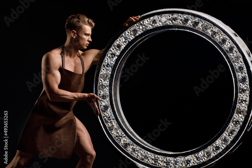 Fotografía A stylish, muscular man with a naked torso makes a piece of jewelry on a dark background