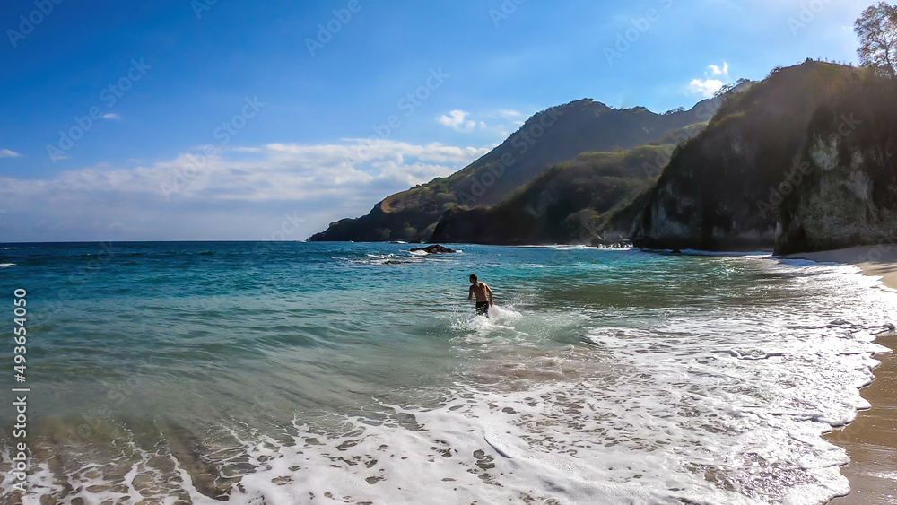 A man jumping into the waves on idyllic Koka Beach. Hidden gem of Flores, Indonesia. He is having a lot of fun, collecting happy moments. Adventure and discovering while travelling