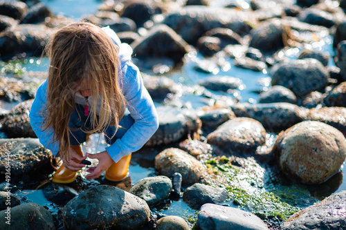 A young girl in rubber boots plays in rocks and water on the coast of Alaska