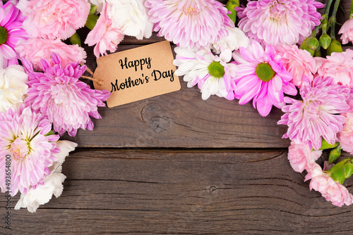 Happy Mothers Day gift tag with arch border of pink, purple and white flowers. Top view on a dark wood background. Copy space.