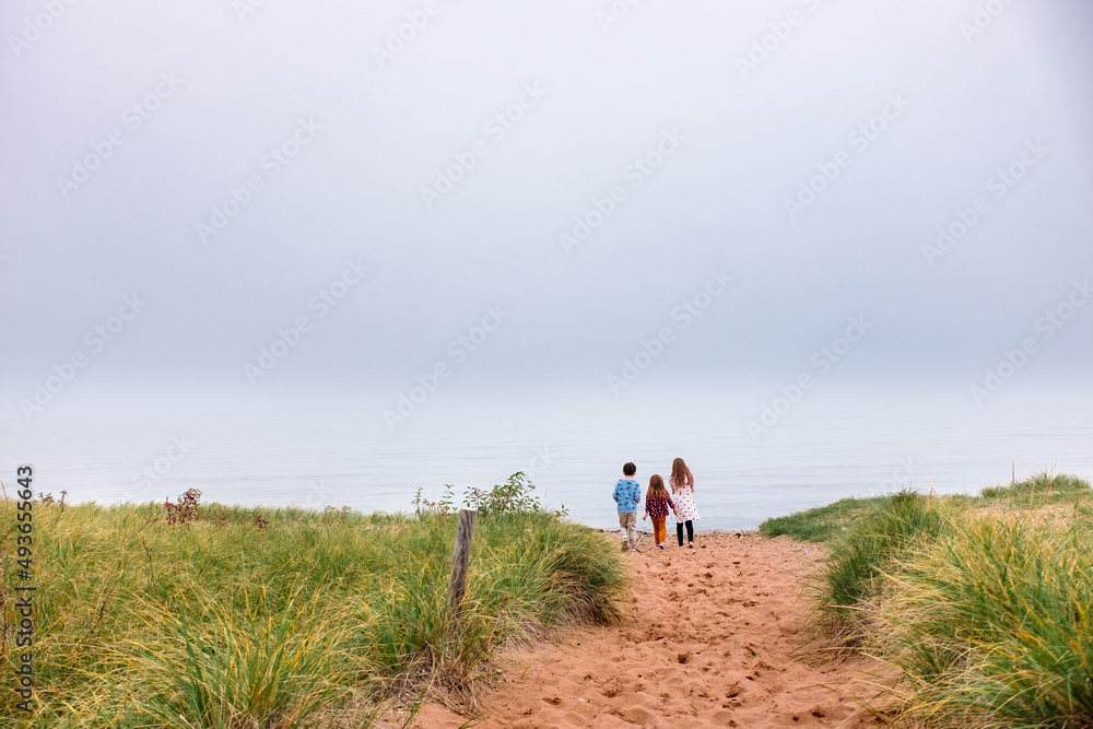 Three children walk up a sandy path toward water on a foggy day near Lake Superior Three children walk up a sandy path toward water on a foggy day near Lake Superior
