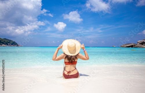 back view of woman wearing a straw hat and orange bikini relax on the beach with beautiful blue sky.at Similan island Phuket Thailand   summer vacation concept