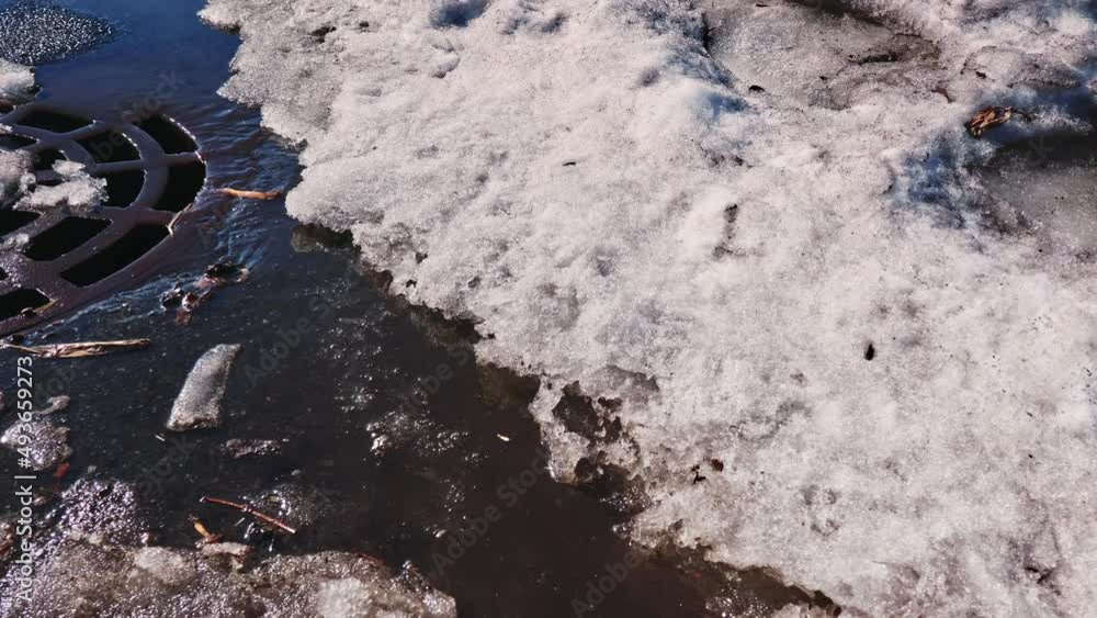 Rapid flow of meltwater runs on the road with melted snowdrifts into the storm sewer. Rapid flow of meltwater runs on the road with melted snowdrifts into the storm sewer.