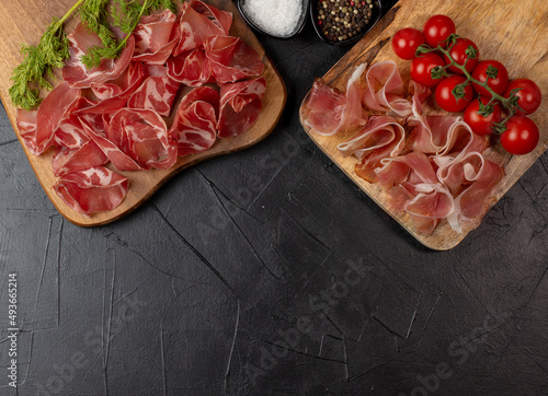 Prosciutto crudo parma ham, dry cured pork meat on a wooden board. Black background. Copy space. Banner space for your text