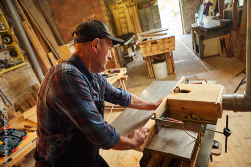 Senior carpenter in uniform works on a woodworking machine at the carpentry manufacturing