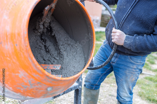 Man busy doing masonry work, mixing concrete with an electric cement mixer, wheelbarrow and shovel. bonus 110%, superbonus.
