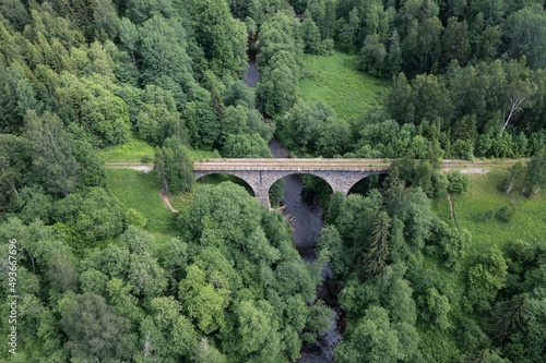 Stone bridge over small river on abandoned section of old railway overgrown with grass and trees