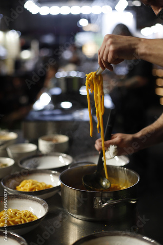 Chef trabajando en cocina un plato de pasta con salsa elev  ndola con un tenedor en sus manos
