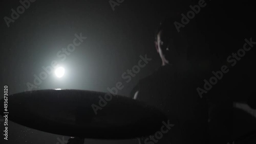the drummer's silhouette hitting the cymbal with his sticks in slow motion. the water splashes in different directions