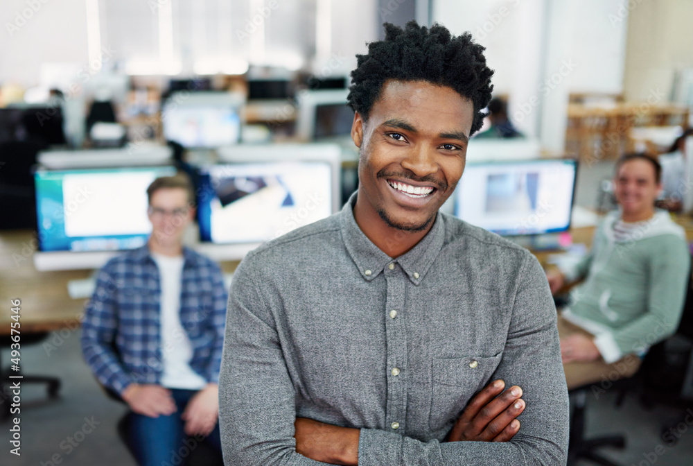 Fototapeta premium We turn ideas into reality. Portrait of a young man standing in an office with designers in the background.