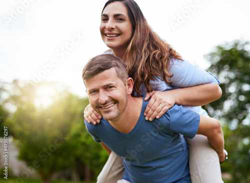 Our love prospers on. Shot of a cheerful young man giving his wife a piggyback ride outside in a park during the day.