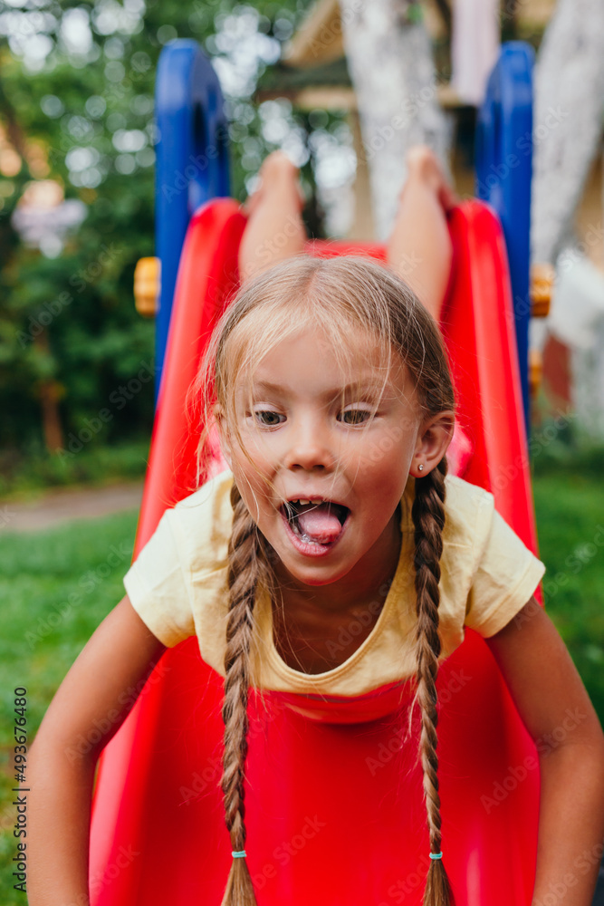 Funny little girl playing on a slide at a playground. Childhood. Funny little girl playing on a slide at a playground. Childhood.