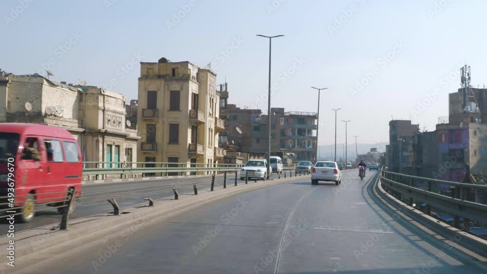Car drives along bridge road of Cairo in sunny day. View from inside automobile. Urban architecture of modern arab city. Egyptian cityscape with houses, buildings, mosque, trees, street lamps Car drives along bridge road of Cairo in sunny day. View from inside automobile. Urban architecture of modern arab city. Egyptian cityscape with houses, buildings, mosque, trees, street lamps