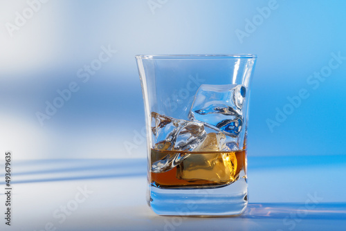 Glass of amber scotch whiskey and ice on a bright background
