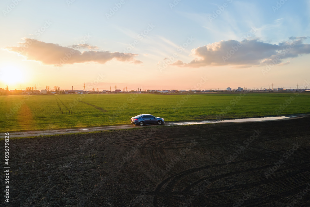 Aerial view of sedan car driving fast on dirt road at sunset. Traveling by vehicle concept Aerial view of sedan car driving fast on dirt road at sunset. Traveling by vehicle concept