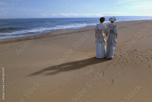 Two women in victorian fashion strolling along a beach