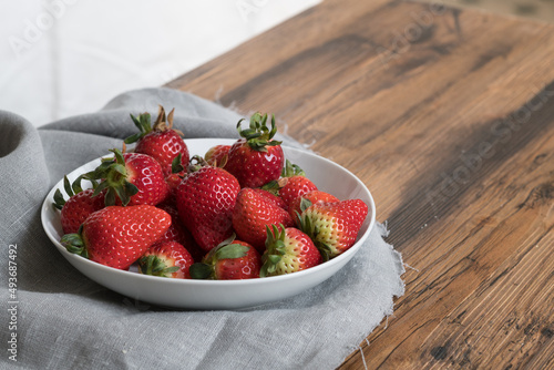 Ripe red strawberries in white bowl on old wooden table