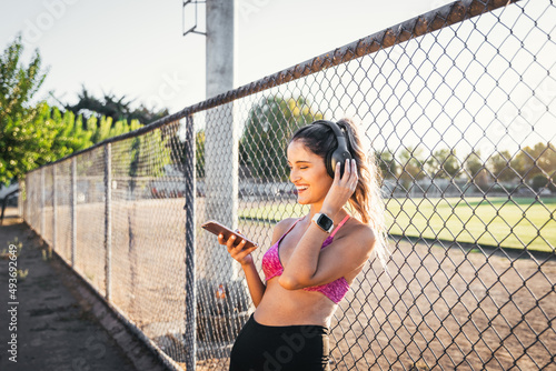 Young active woman laughing, using wireless headphones and setting a music playlist on her smartphone before work out
