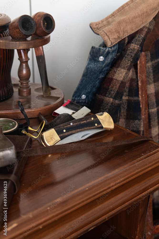 Pocket folding knife lying on table with compass in front of denim work coat