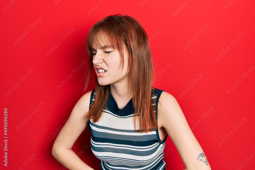 Redhead young woman wearing casual t shirt with hand on stomach because nausea, painful disease feeling unwell. ache concept. Redhead young woman wearing casual t shirt with hand on stomach because nausea, painful disease feeling unwell. ache concept.