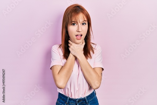 Redhead young woman wearing casual pink t shirt shouting and suffocate because painful strangle. health problem. asphyxiate and suicide concept.