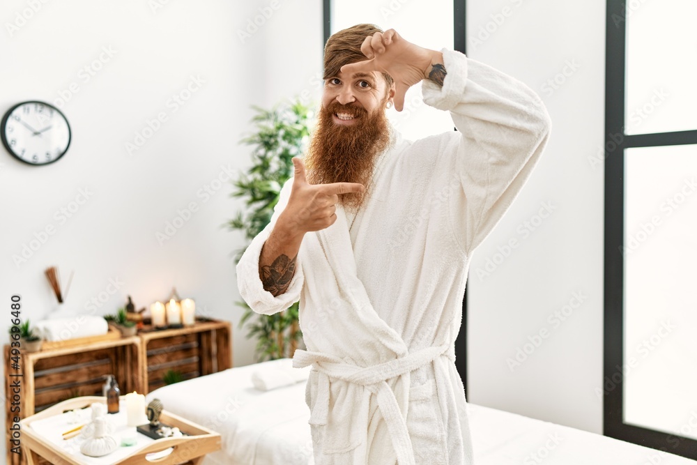 Redhead man with long beard wearing bathrobe at wellness spa smiling making frame with hands and fingers with happy face. creativity and photography concept. Redhead man with long beard wearing bathrobe at wellness spa smiling making frame with hands and fingers with happy face. creativity and photography concept.