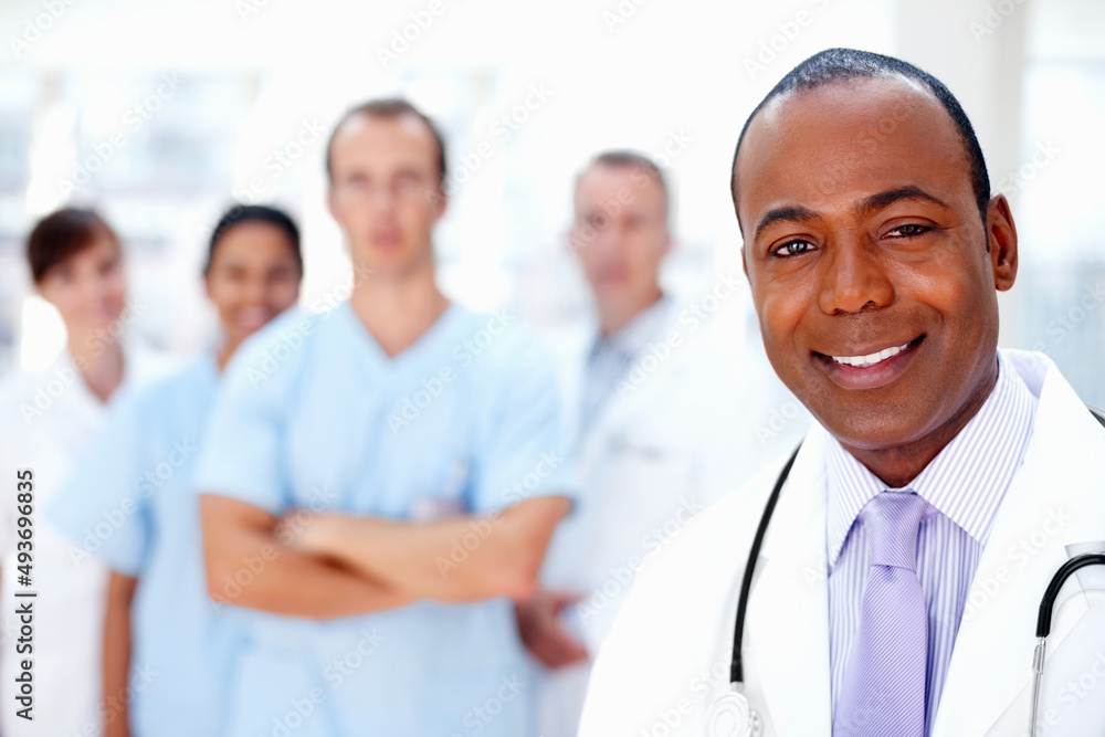 Confident doctor with medical team in background. Focus on doctor with colleagues in background. Confident doctor with medical team in background. Focus on doctor with colleagues in background.