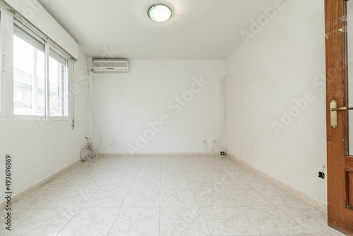 Empty living room with light glossy stoneware floor  large aluminum window  wooden door  ceiling light fixture and air conditioning