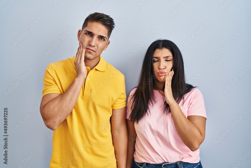 Fototapeta premium Young couple standing over isolated background touching mouth with hand with painful expression because of toothache or dental illness on teeth. dentist