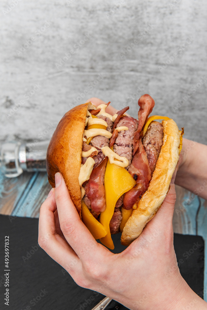 holding in two hands a monster tri-meat beef burger with lots of fried bacon  and cheddar cheese with sauces Photos | Adobe Stock