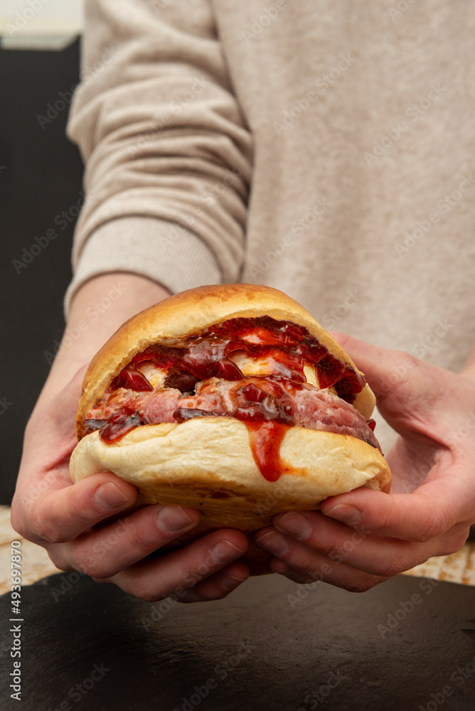Delicious beef burger with goat cheese and lots of spicy tomato jam held in two hands Delicious beef burger with goat cheese and lots of spicy tomato jam held in two hands